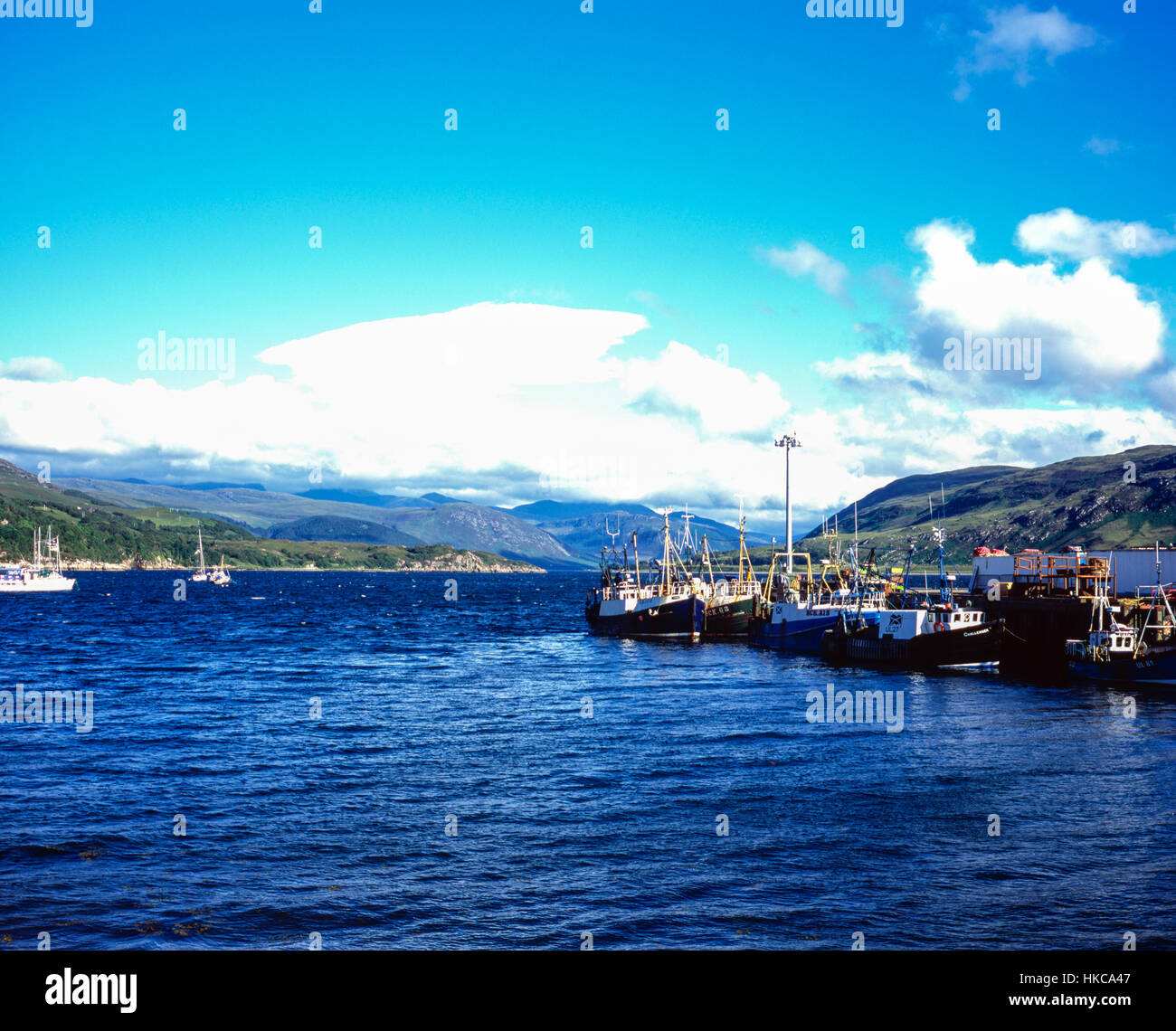 View of fishing boats moored in Loch Broom at Ullapool with Lenticular cloud passing across Beinn Dearg  Wester Ross Scotland Stock Photo