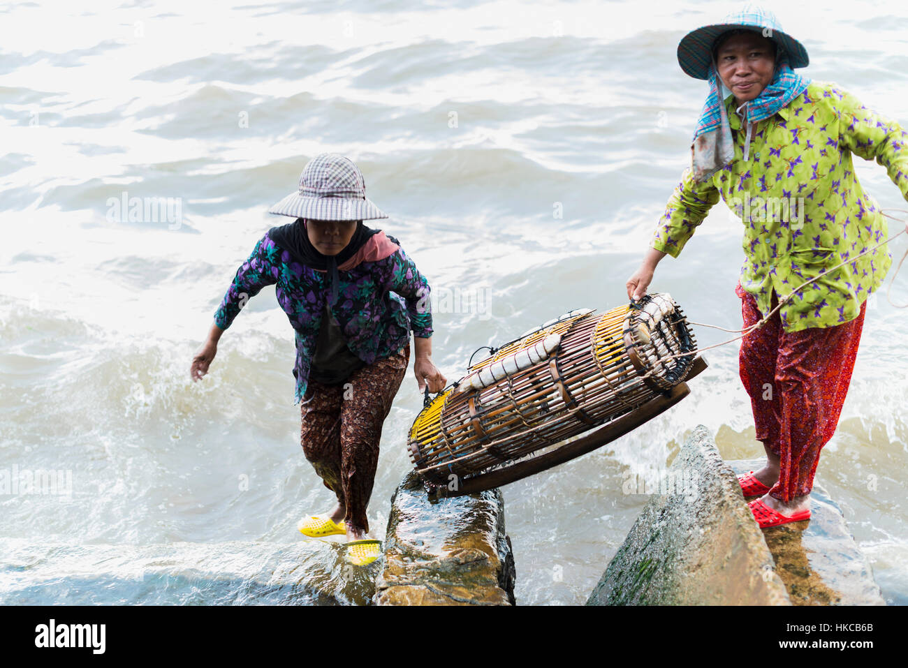 Women carrying a large crab trap from the water, local life in the famous crab market; Kep, Cambodia Stock Photo