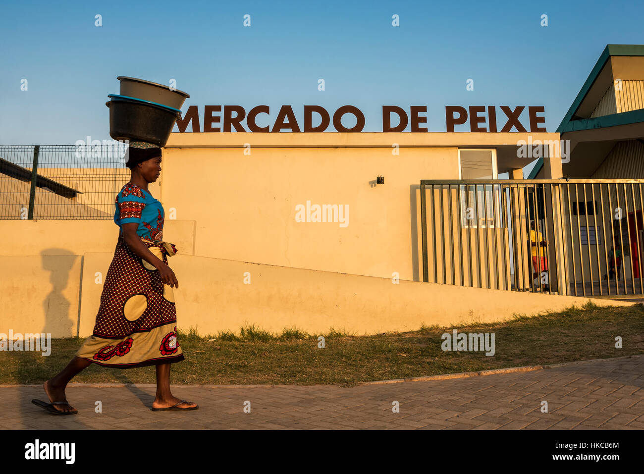 Mozambican woman in traditional capulana dress carrying pails on her head; Maputo, Mozambique Stock Photo