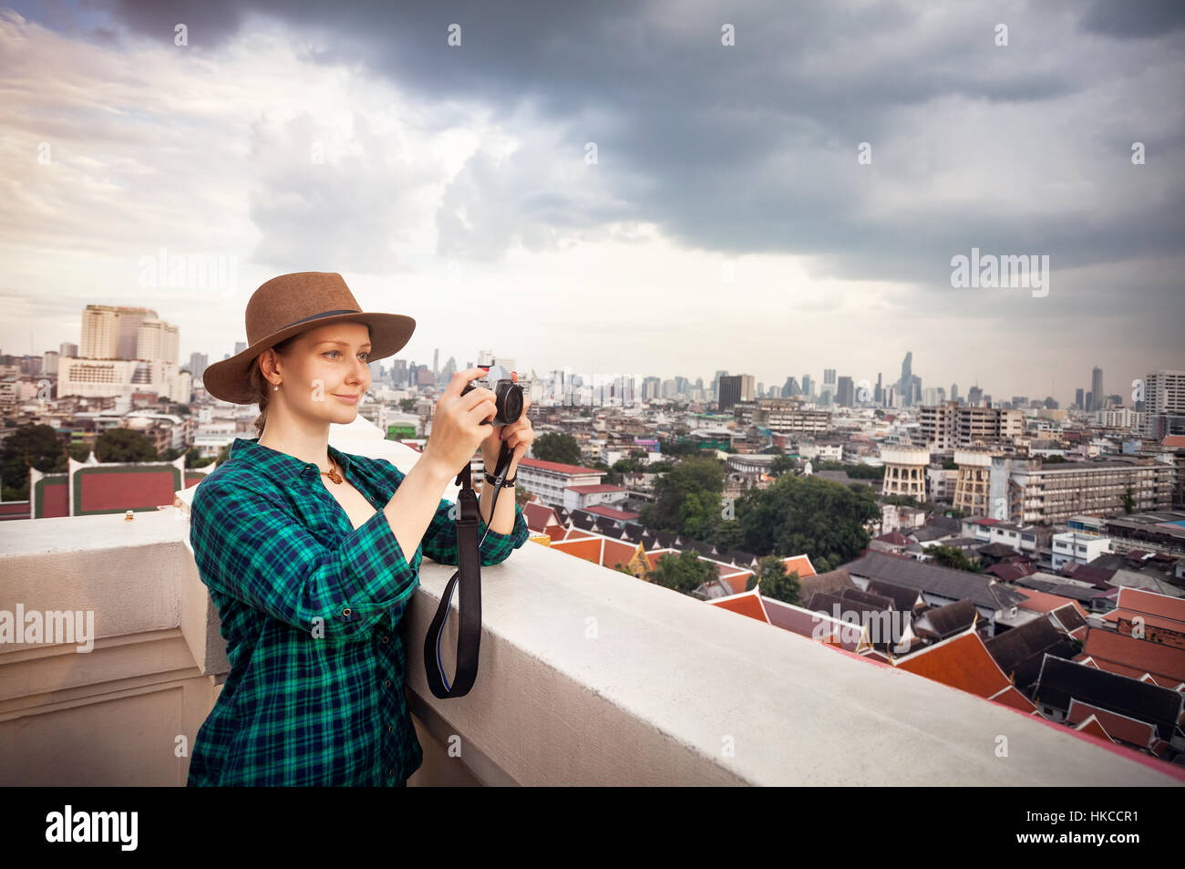 Tourist woman taking pictures with retro style camera at Bangkok City panorama with skyscrapers of business district from Golden Mountain Wat Saket ro Stock Photo