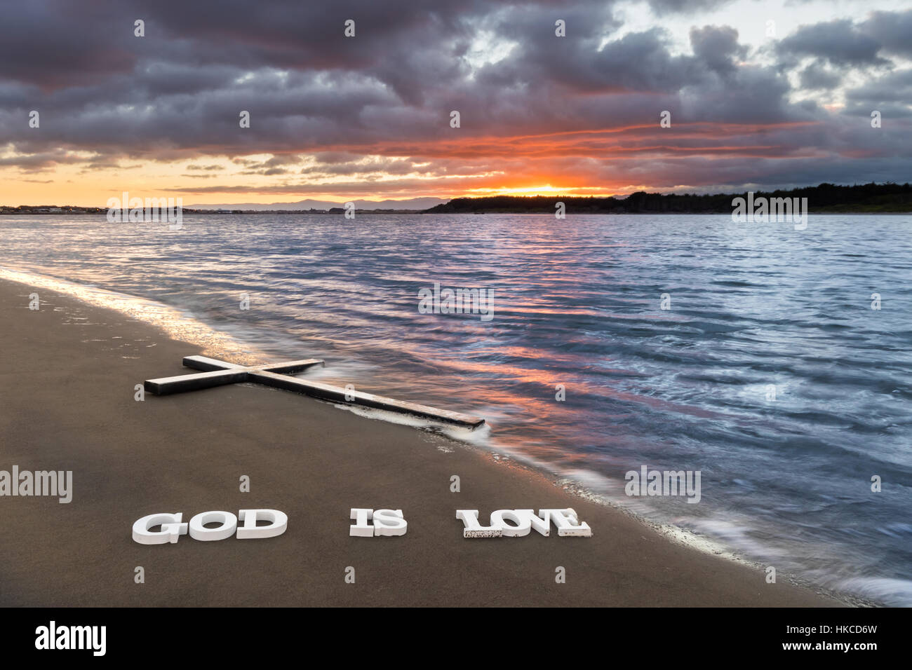 Cross on a river beach with the words 'God is Love' below it. Stock Photo
