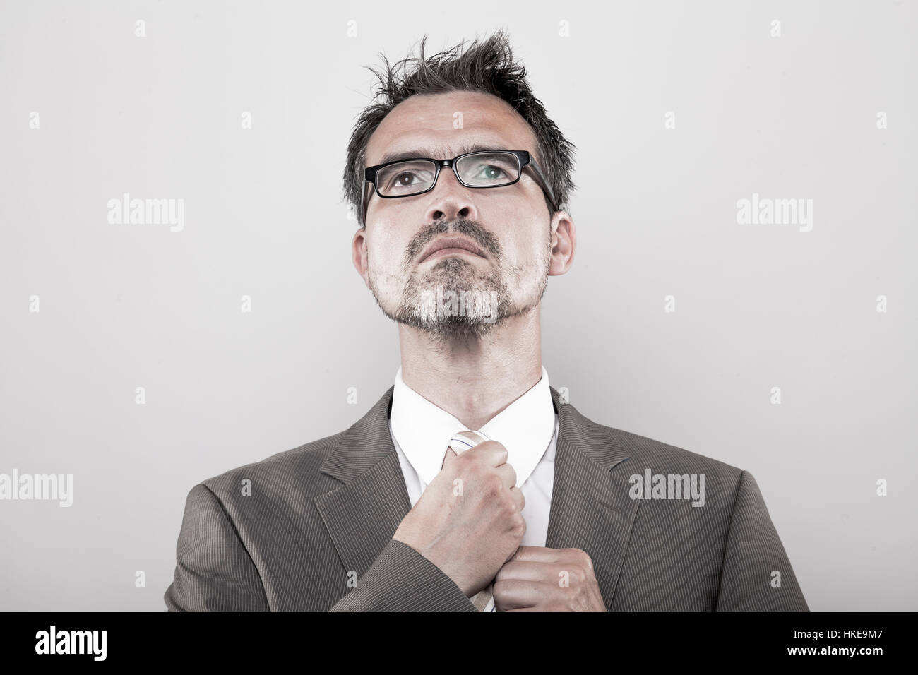 Manager in pinstripe jacket ties his tie looking upwards Stock Photo