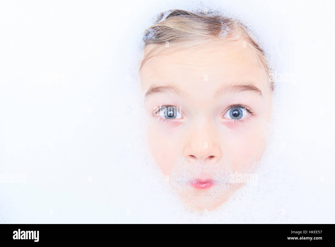 Funny little child blond girl in a bubble bath filled with soap foam