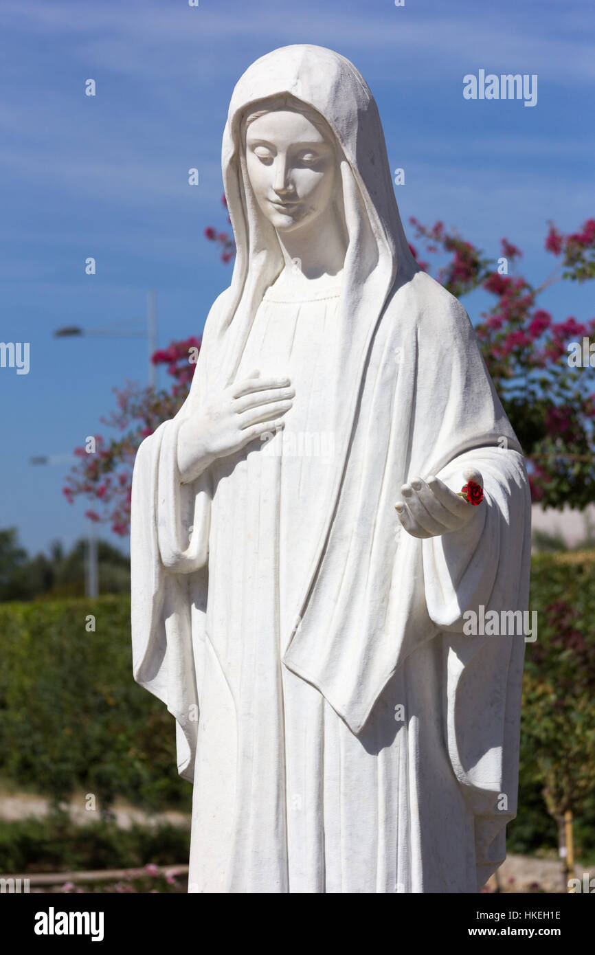 Statue of Virgin Mary in front of the church of Saint James. She is inviting her children to pray. MEDJUGORJE, BOSNIA AND HERZEGOVINA, 2016/08/20. Stock Photo
