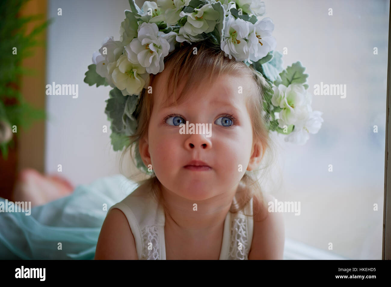 Beautiful little girl in a wreath on the head in green and white. Party ...