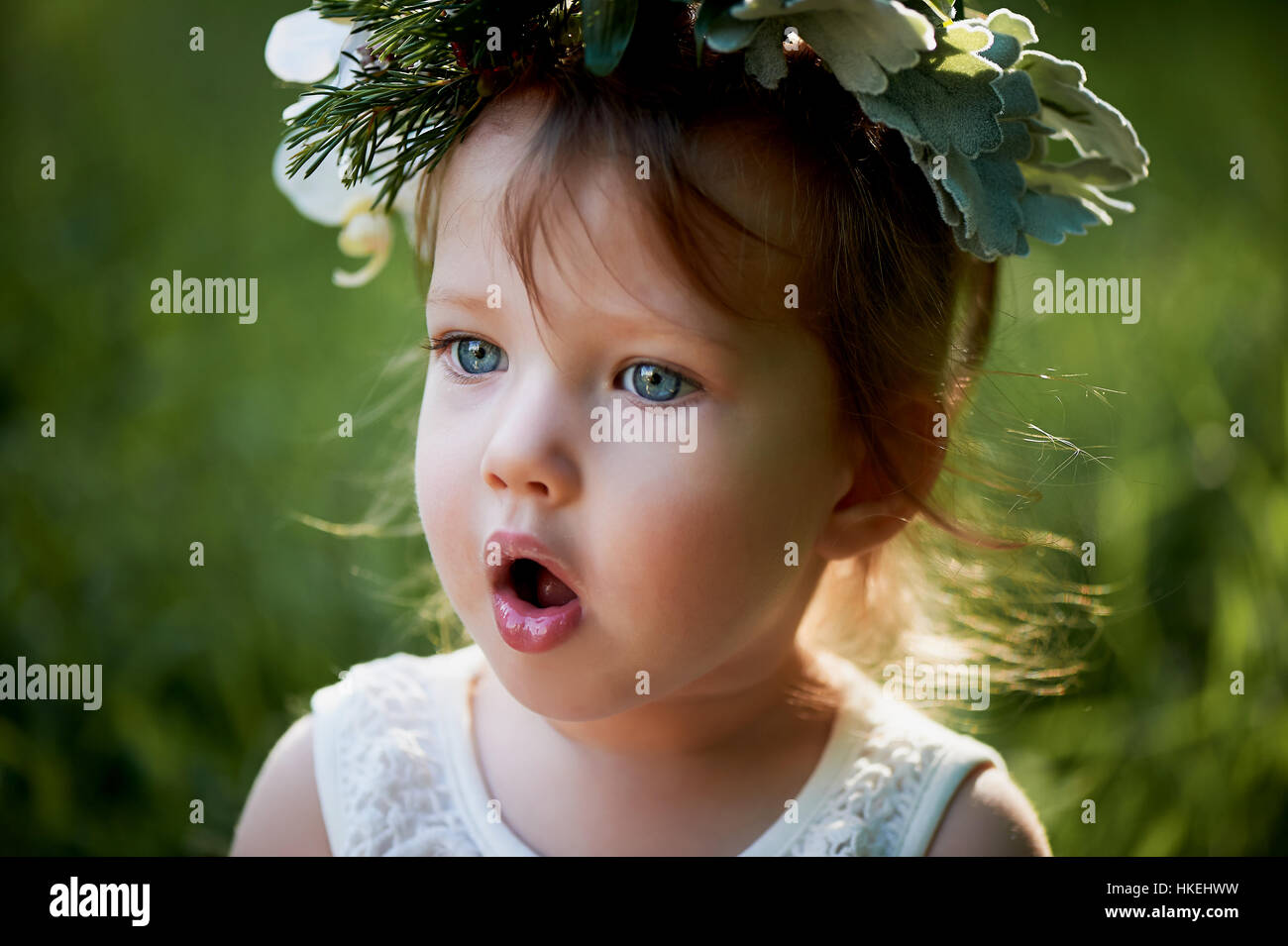 Beautiful little girl in a wreath on the head in green and white. Dress ...