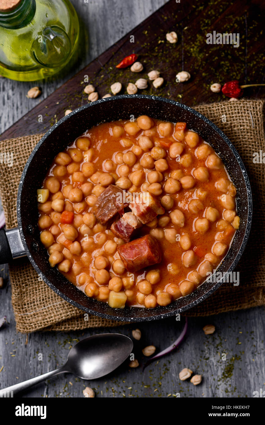 high-angle shot of a stone frypan with garbanzos a la riojana, a spanish chickpeas stew, on a wooden chopping board placed on a rustic wooden table ne Stock Photo