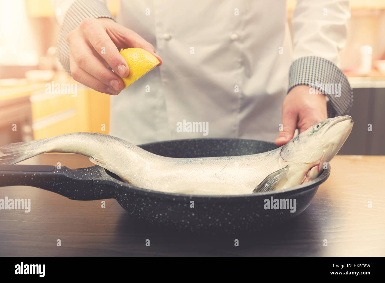 chef squeeze lemon over salmon fish in pan Stock Photo