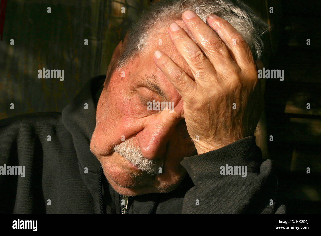 Portrait of old man napping while sitting outside in the sun Stock