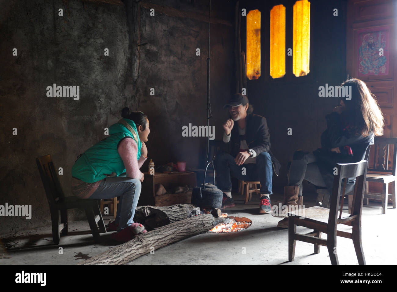 Guests at a farmhouse in a village in the mountains of west China sit in the living room with their host around an open log fire for warmth. Stock Photo