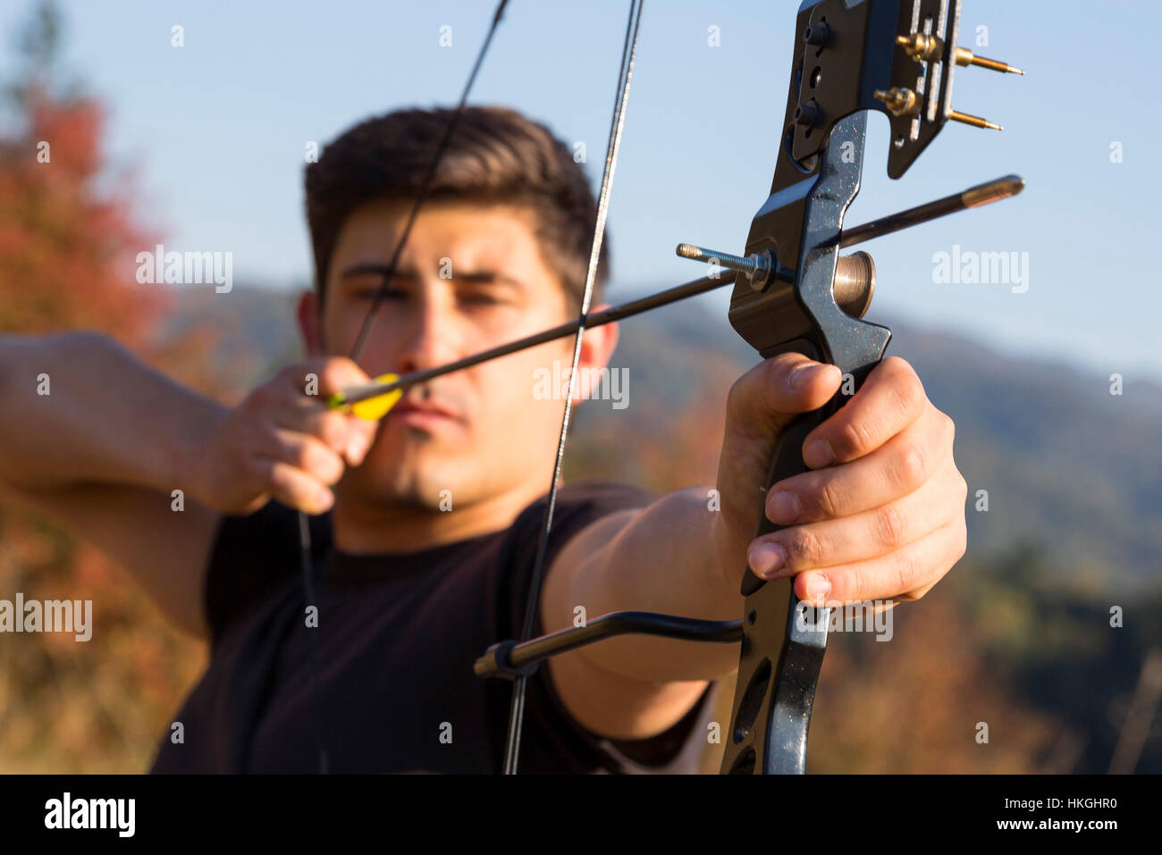 An archer draws his compound bow and aims upwards with clean blue sky