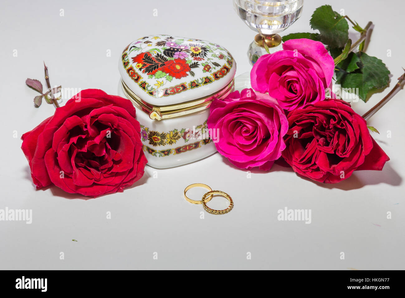 Romantic heart shaped embroidered jewelry box with bright red and pink roses with gold engagement rings for Valentines day. Stock Photo