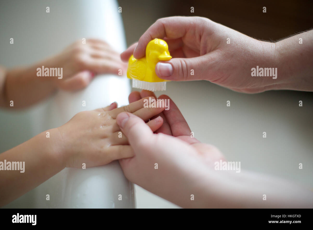 parent's hand cleaning kid's fingernail at the edge of bathtub. childhood, hands, nail brush, duck. Stock Photo
