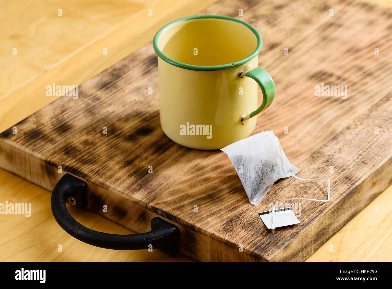 Paper tea bag with yellow and green enameled tea cup on wooden tray with iron handle. Stock Photo