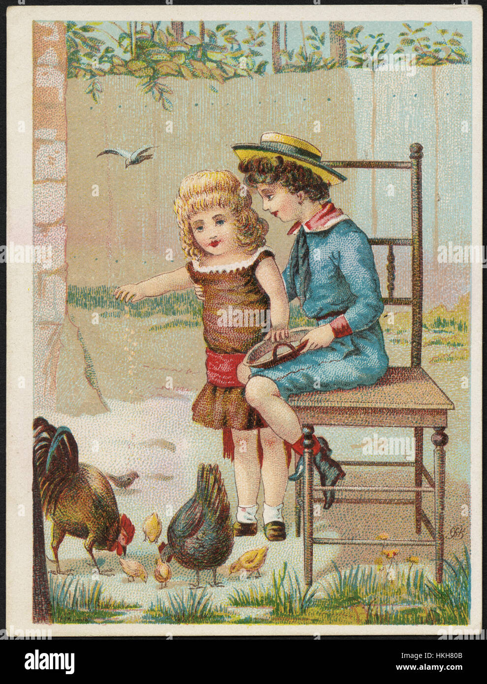 Boy sitting on a chair while a girl stands feeding chickens. Stock Photo