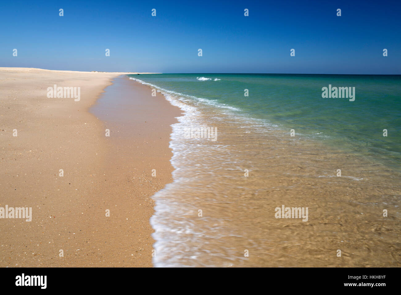 Empty white sand beach and breaking waves of crystal clear sea, Ilha do Farol, Culatra barrier island, Olhao, Algarve, Portugal Stock Photo