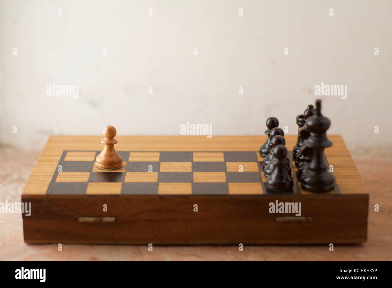 A half chess board with chess pieces arranged showing one white pawn against many black pieces Stock Photo