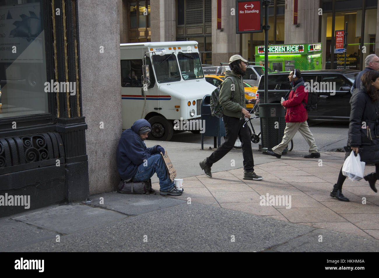 People pass by a homeless man sitting on the sidewalk begging, such a common site in Manhattan that people often hardly notice. Stock Photo