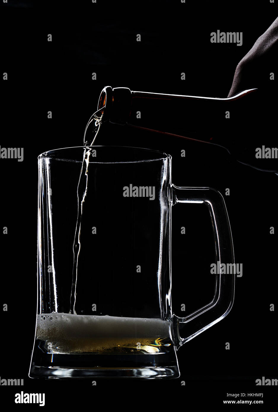 Serving beer in empty glass from bottle on black Stock Photo
