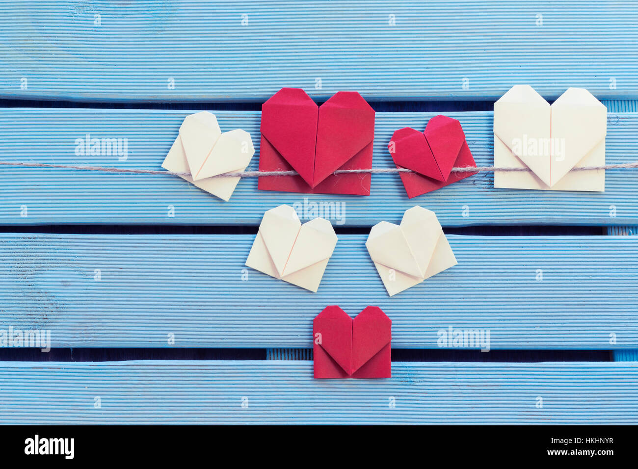Origami hearts bookmark hanging on blue wooden background. Subject captured against soft window lighting on a blue wooden background. Copy Space. Stock Photo