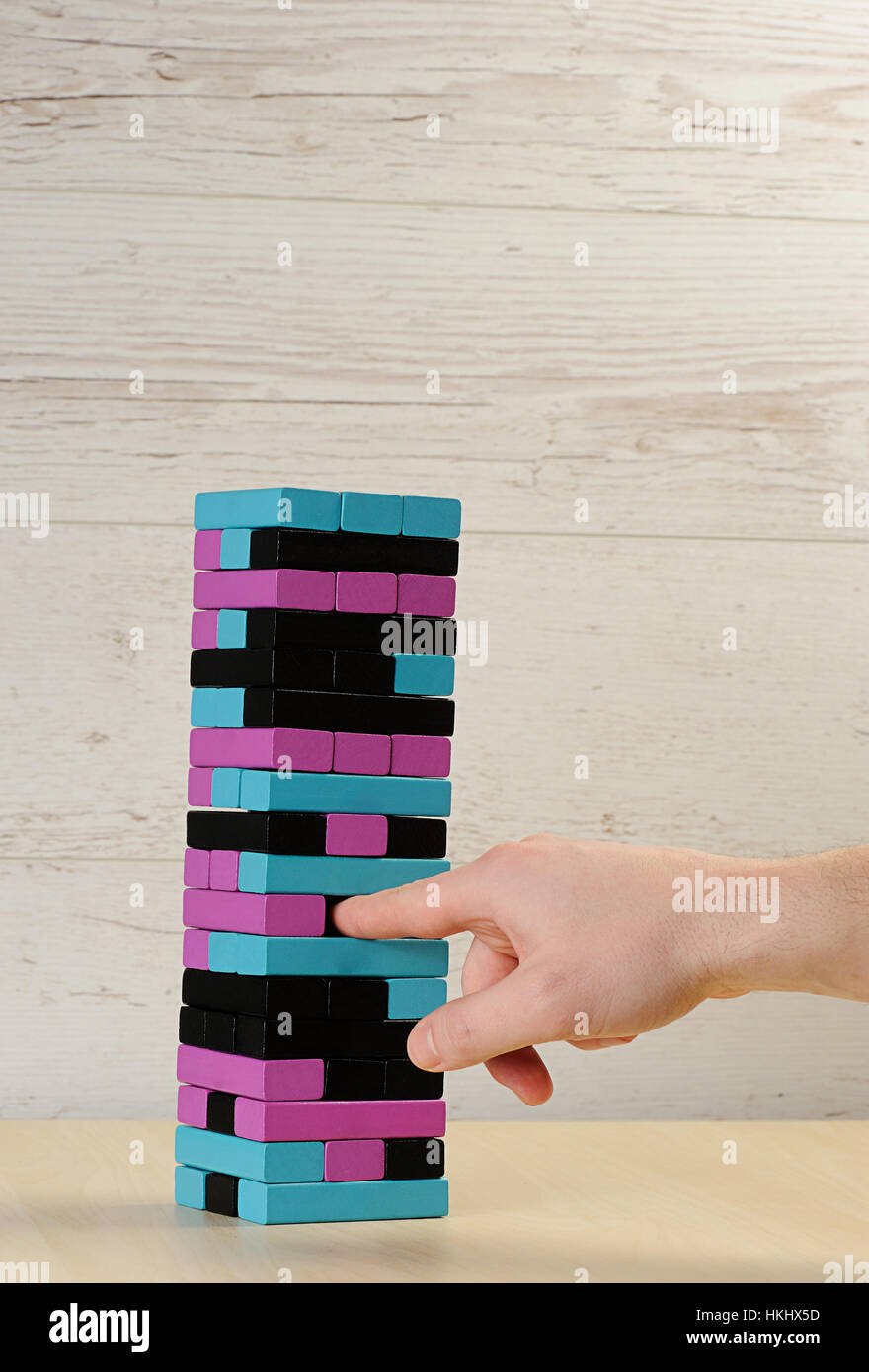 pull jenga tower brick colour on wood table with hand Stock Photo