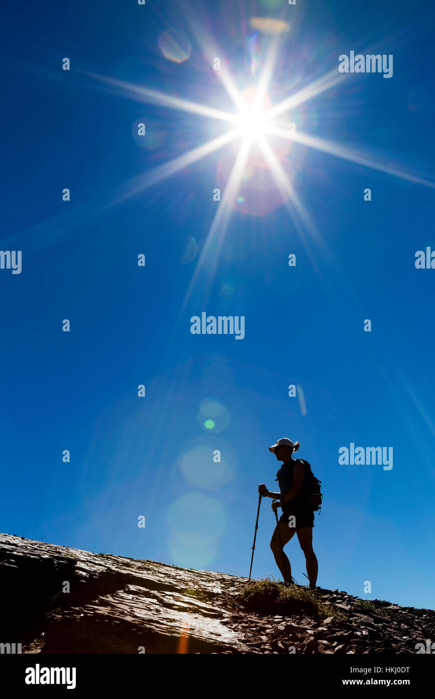 Silhouette of female hiker on rocky ridge with blue sky and sunburst ...