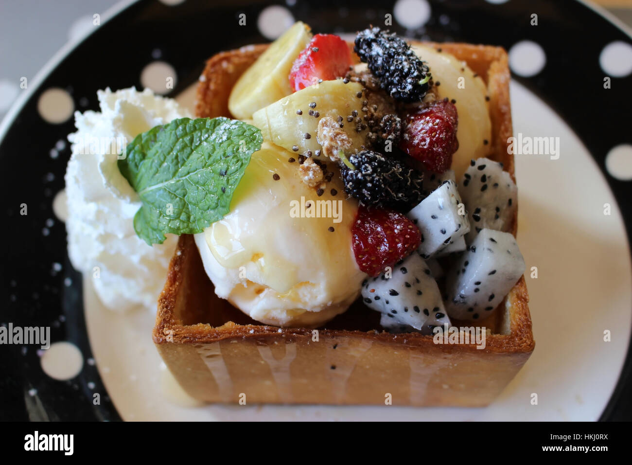 Honey Toast with Exotic Tropical Fruits such as Dragon Fruit and Banana topped off with ice cream and a mint leaf Stock Photo