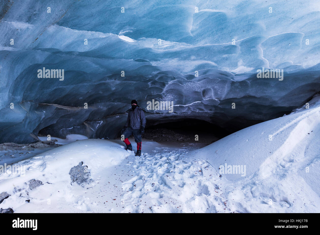A man poses in front of a cave at the terminus of Fels Glacier (commonly misspelled 'Eel' Glacier) in the Alaska Range in winter Stock Photo