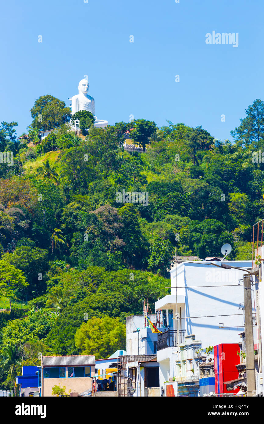 The distant, white Bahiravokanda Vihara Buddha Statue seen from below at street or ground level sits atop a hill in Kandy Stock Photo