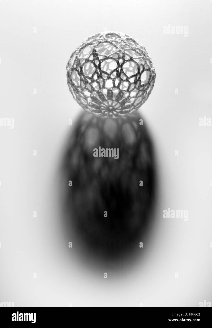 Grey sphere with openwork pattern shell casting long shadow over white surface, isolated on white background Stock Photo