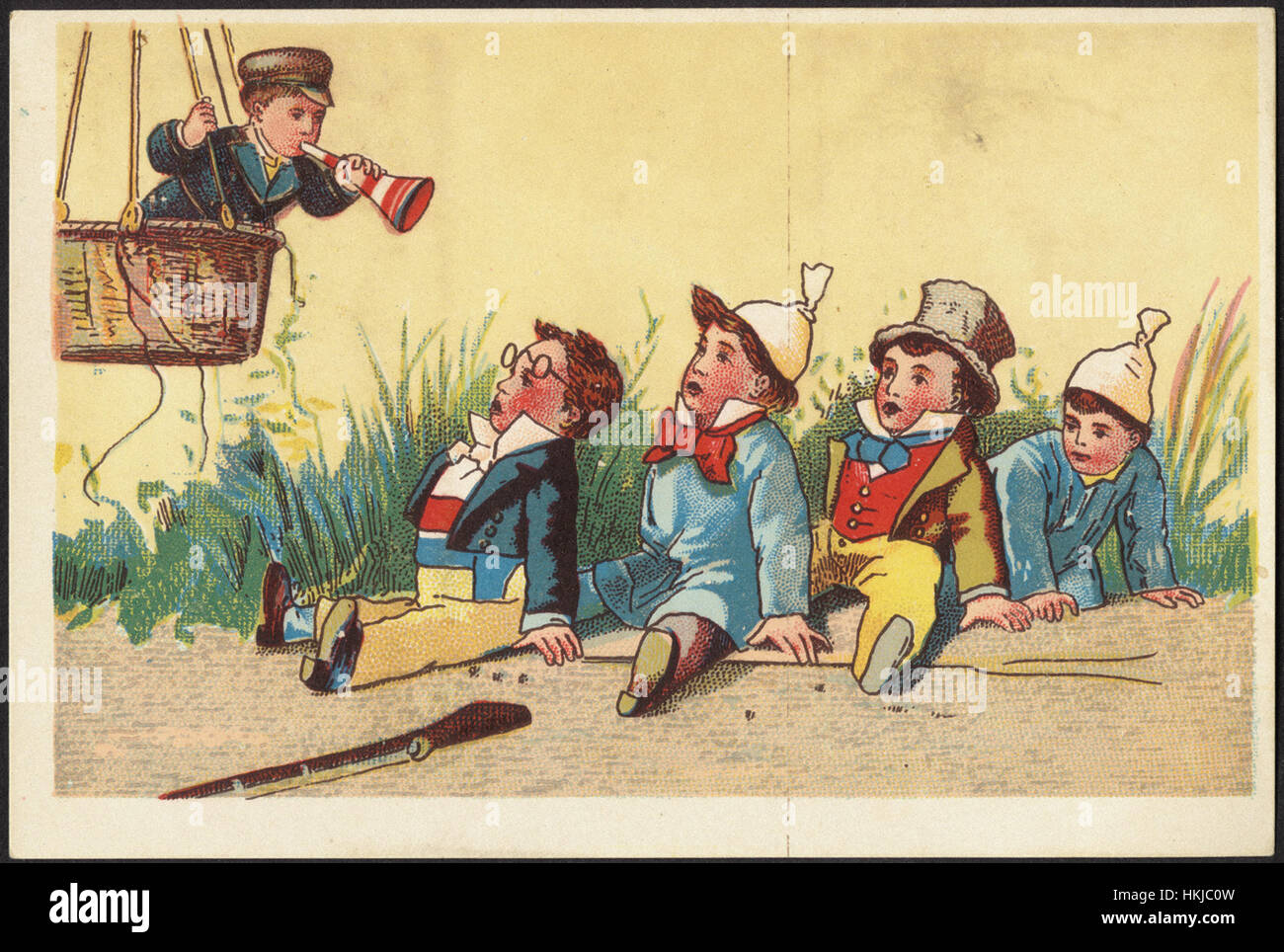 Five boys, four sitting and looking upwards at a boy in the basket of a hot air balloon blowing a horn. Stock Photo