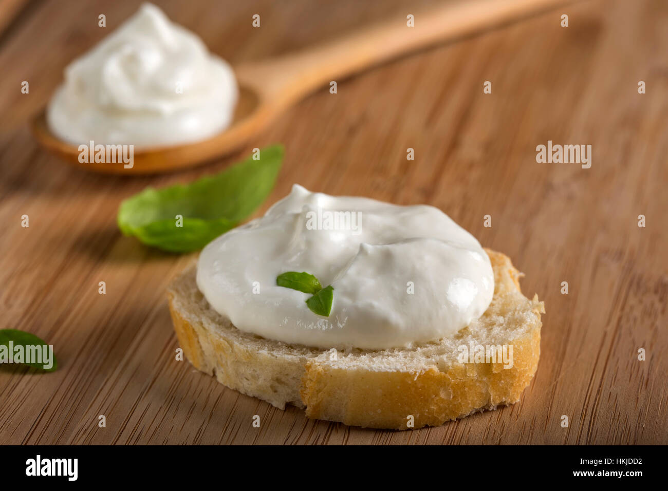 Cream-cheese and basil on french bread over wood background Stock Photo