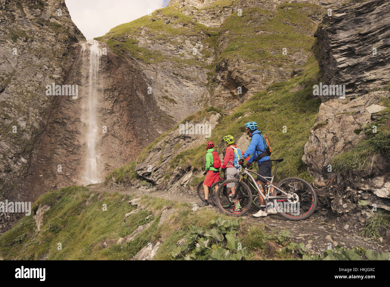 Three mountain biker friends watching waterfall, Zillertal, Tyrol, Austria Stock Photo
