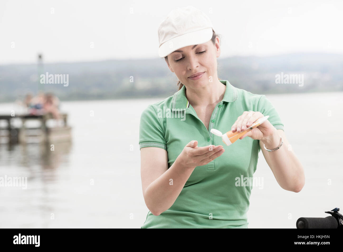 Mature woman applying sun cream by lake, Bavaria, Germany Stock Photo