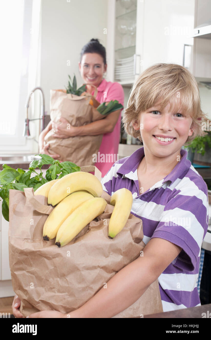 Boy with his mother holding bags of groceries in kitchen,Bavaria,Germany Stock Photo