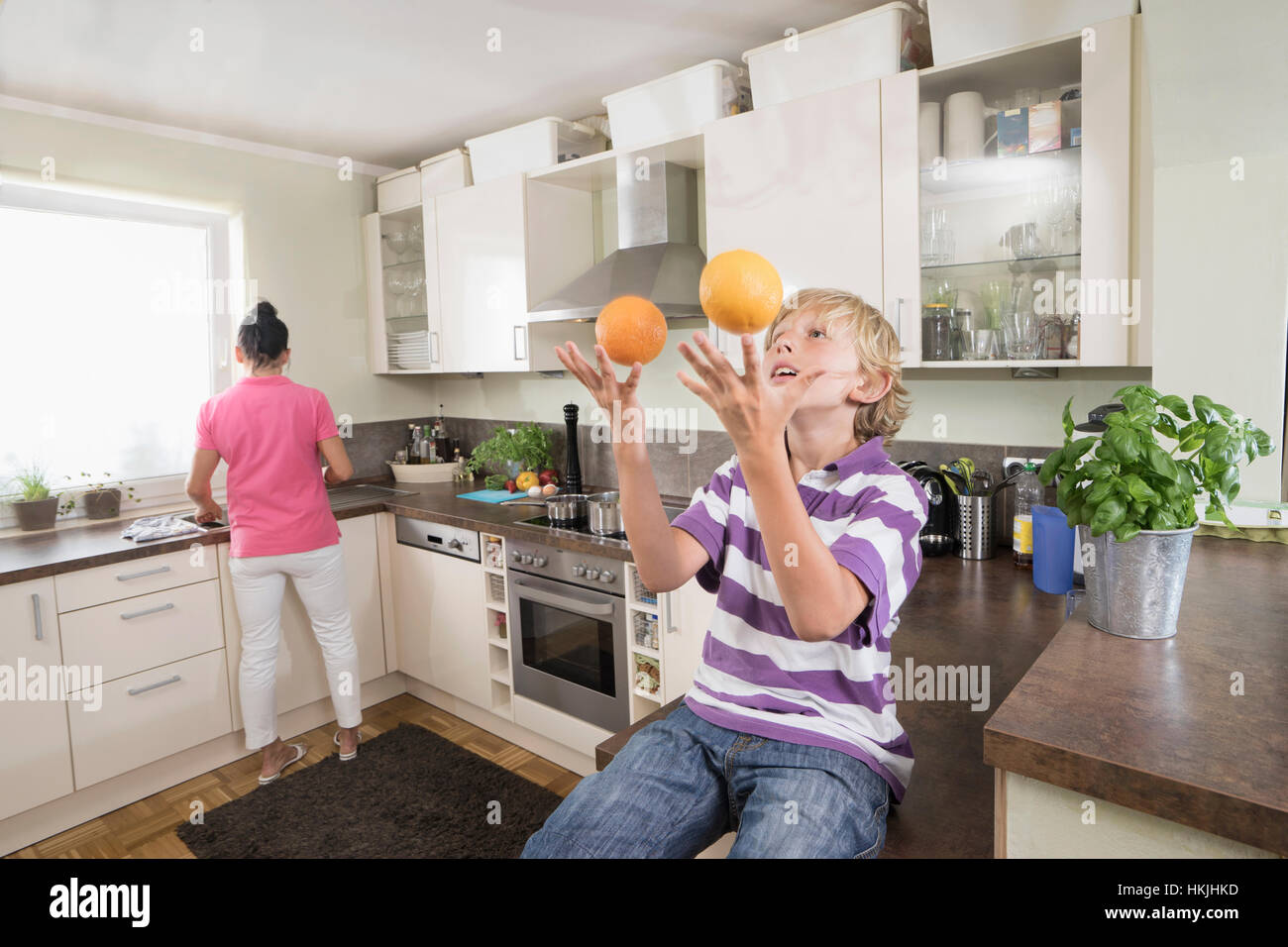 Boy juggling with oranges while mother preparing food,Bavaria,Germany