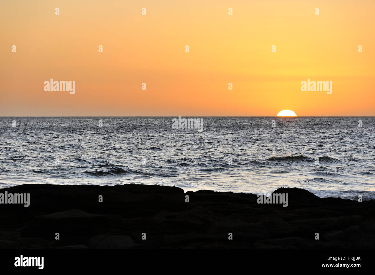 Sun half in horizon of still ocean Stock Photo
