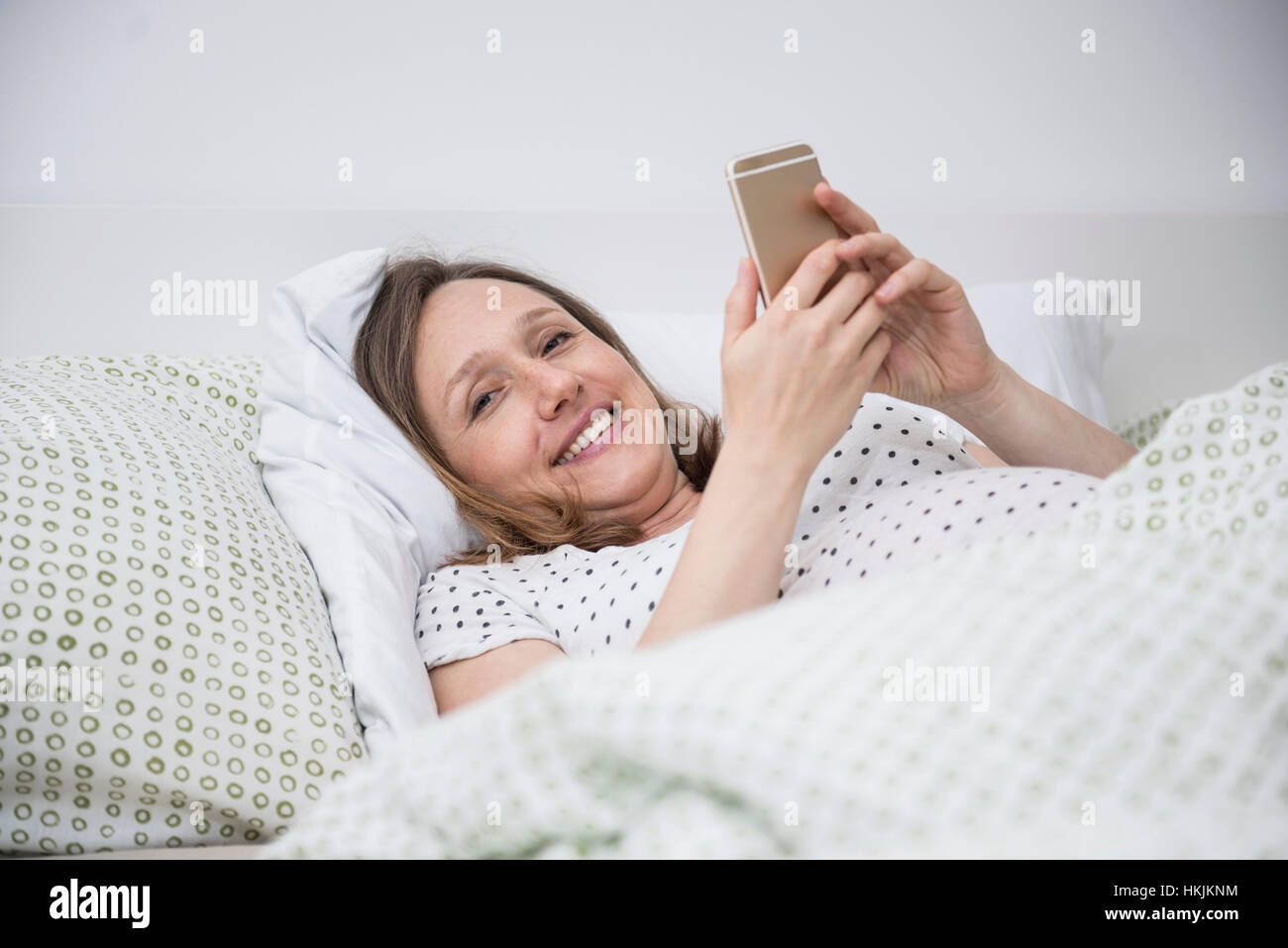 Pregnant woman lying in bed and using on mobile phone, Munich, Bavaria, Germany Stock Photo