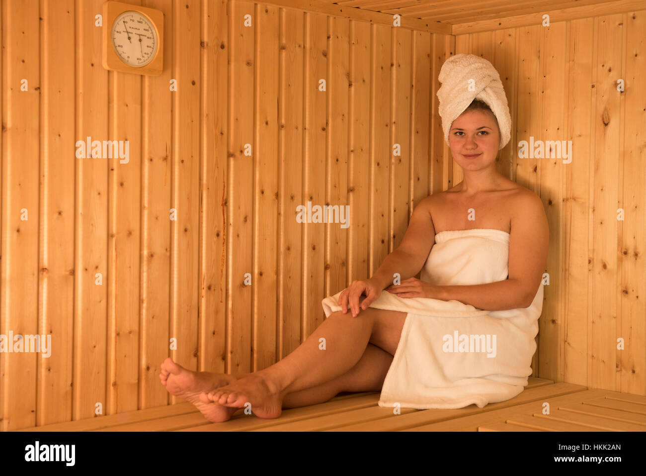 young blond woman in wooden sauna with towel on her head Stock Photo