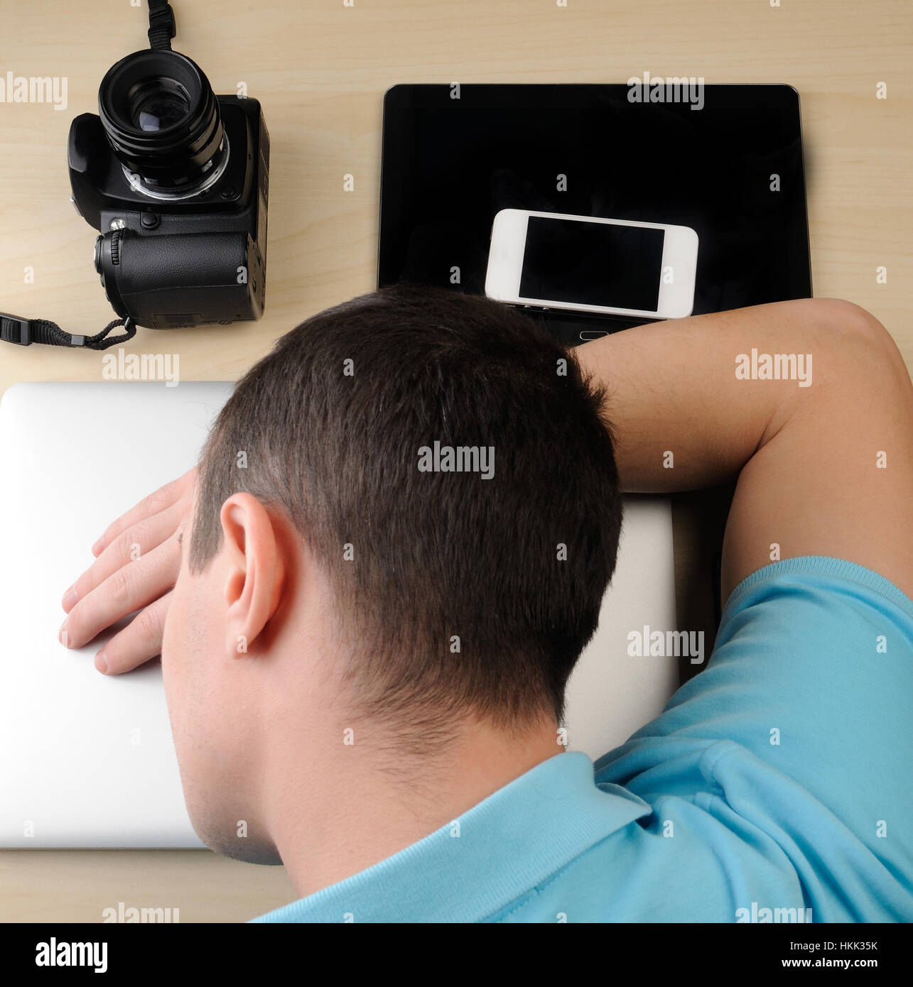 Person sleep on laptop next to camera and tablet on wood table Stock