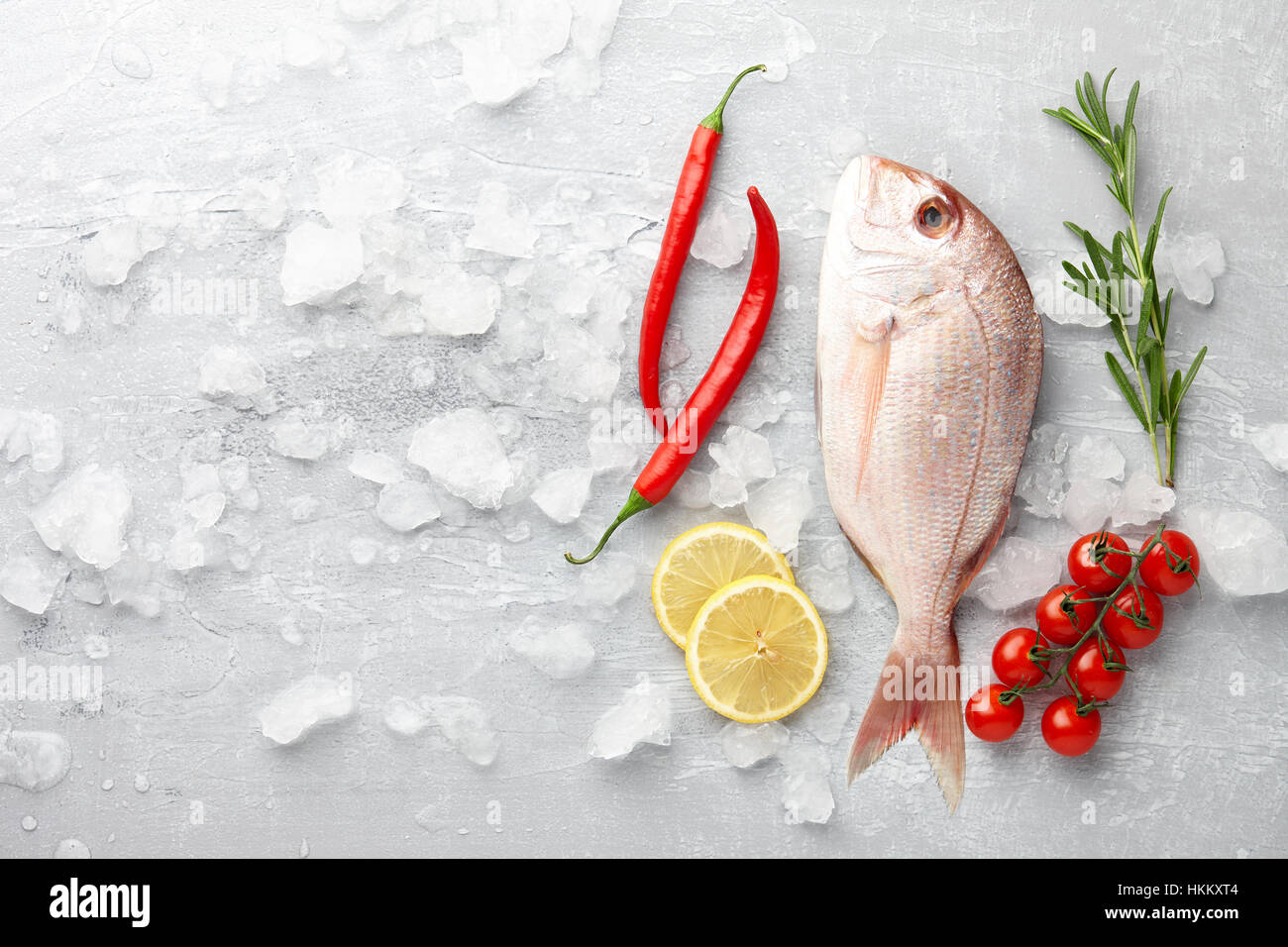 Fish cooking: fresh red Japanese seabream, lemon slices, chili pepper, cherry tomatoes and rosemary on gray stone background Stock Photo