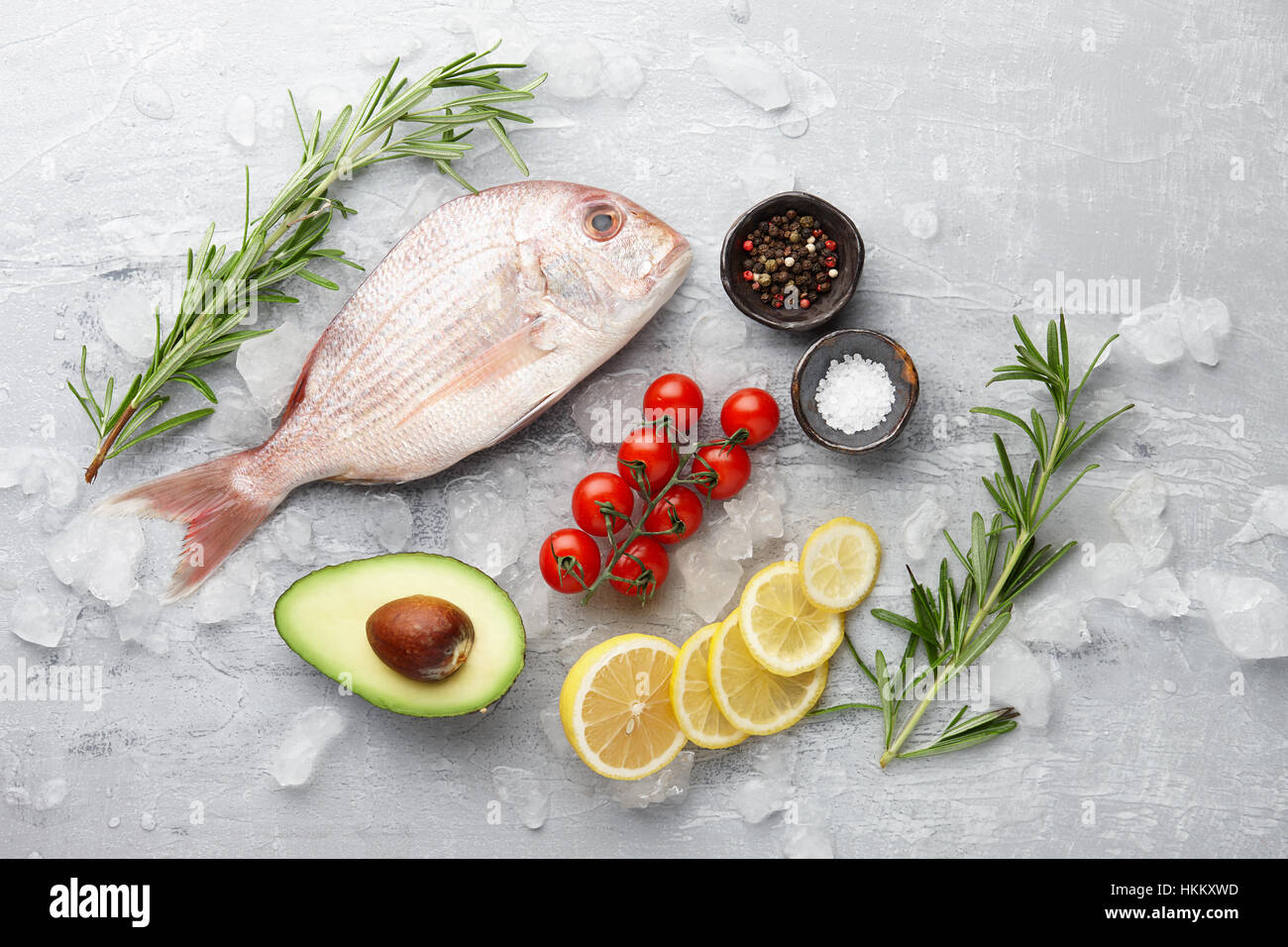 Fish cooking: fresh red Japanese seabream, lemon slices, avocado fruit, chili pepper, cherry tomatoes, olive oil, rosemary and spices on gray stone ba Stock Photo