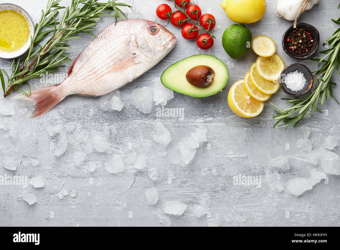 Fish cooking: fresh red Japanese seabream, lemon slices, avocado fruit, chili pepper, cherry tomatoes, olive oil, rosemary and spices on gray stone ba Stock Photo