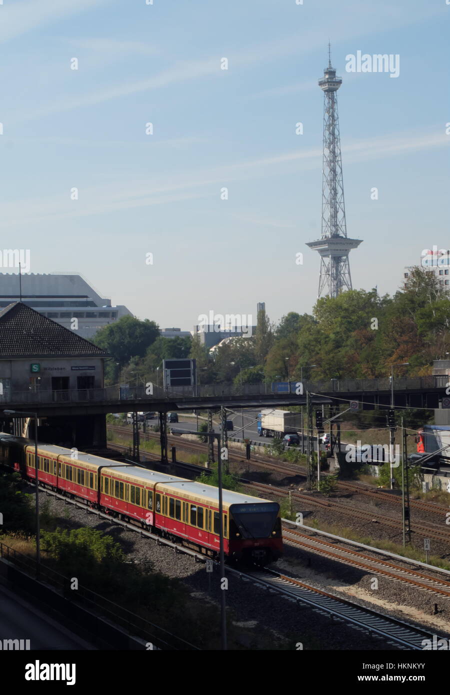 Berlin Funkturm rises behind the Messe Nord S-bahn station as a train leaves the station. Stock Photo