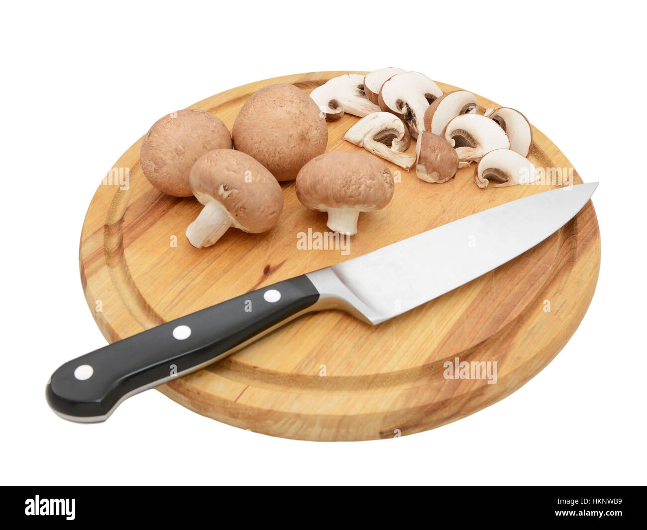 Sharp knife with whole chestnut mushrooms and slices on a circular wooden chopping board, isolated on a white background Stock Photo