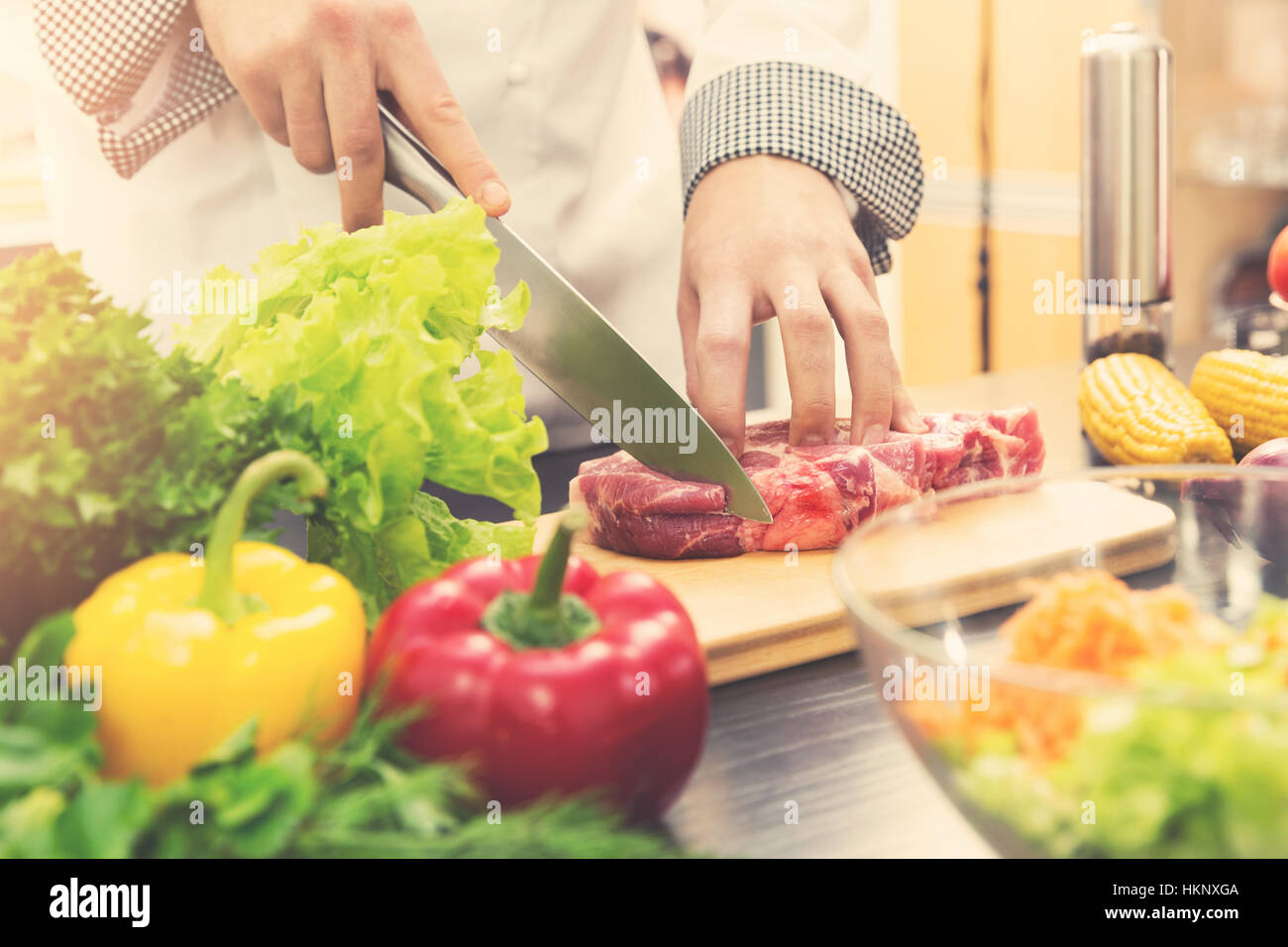 chef cutting raw meat on wooden board in kitchen Stock Photo