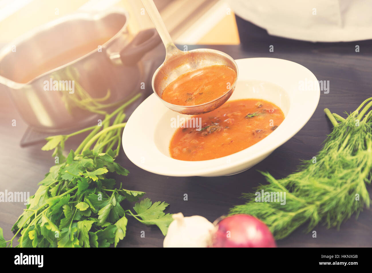 cook pouring soup with ladle into a plate Stock Photo