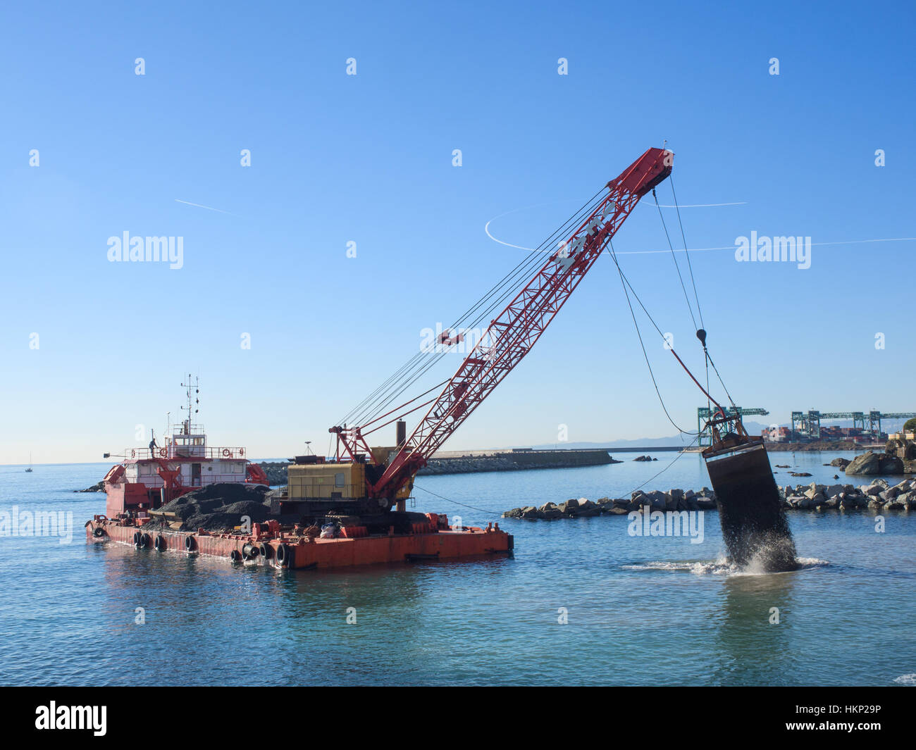 Genoa, Italy   December 22, 2016: Grab Dredge with  Clamshell Bucket unloading gravel in the water of a port next to the shore to replenish a beach Stock Photo