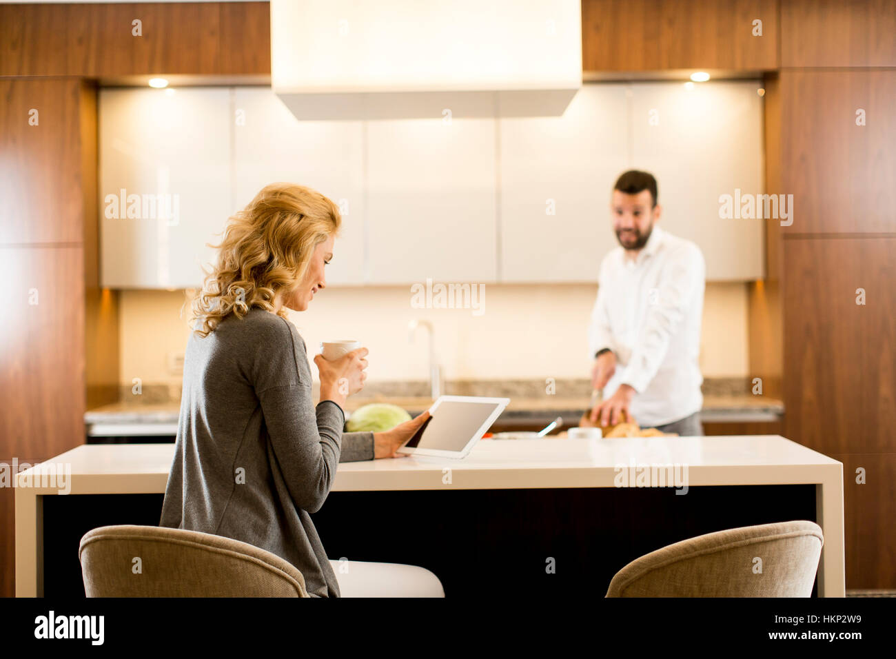 Young woman sits at the kitchen table while man preparing food Stock Photo