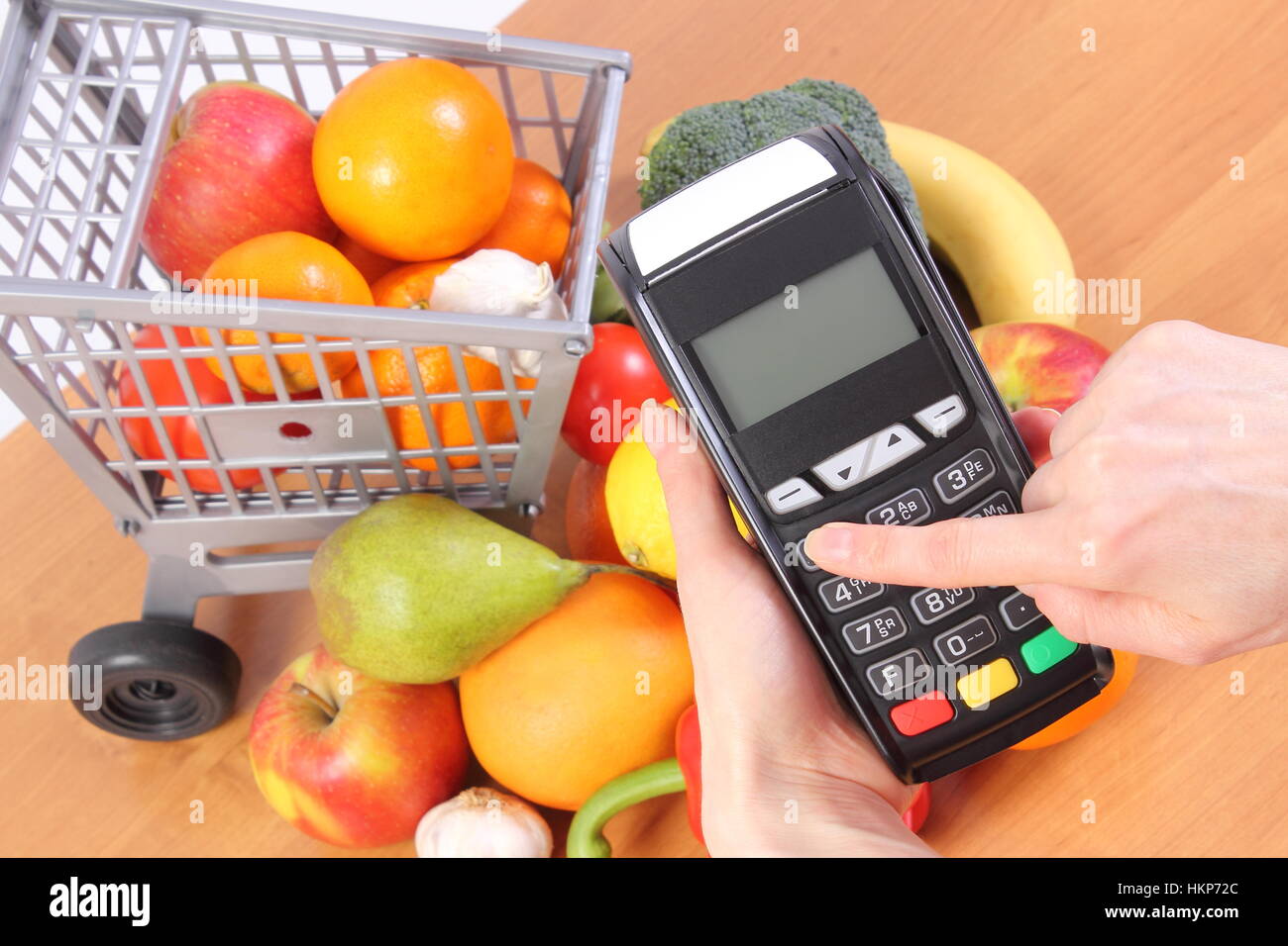 Hand using payment terminal, enter personal identification number, credit card reader and fresh fruits and vegetables with plastic shopping carts, Stock Photo